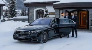 New black Mercedes S-Class 2025 by Limogroup at an upscale, snow-dusted Les Menuires hotel, as a chauffeur assists a client after their premium Geneva to Les Menuires transfer.