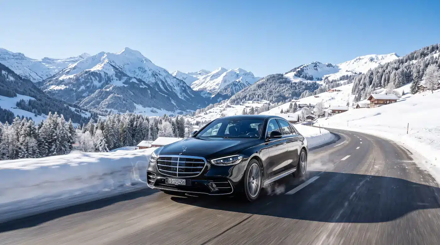 Corporate group transport in Gstaad, Mercedes S-Class on a scenic alpine road with snow-covered mountains